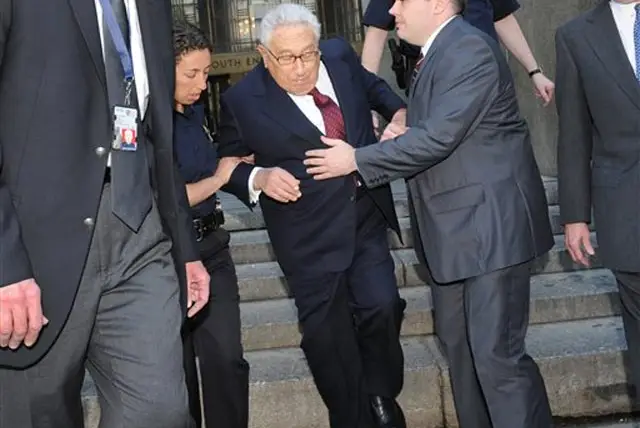 Photograph of former Secretary of State Henry Kissinger being helped up after tripping on the last step of the Manhattan State Supreme Court building by Louis Lanzano